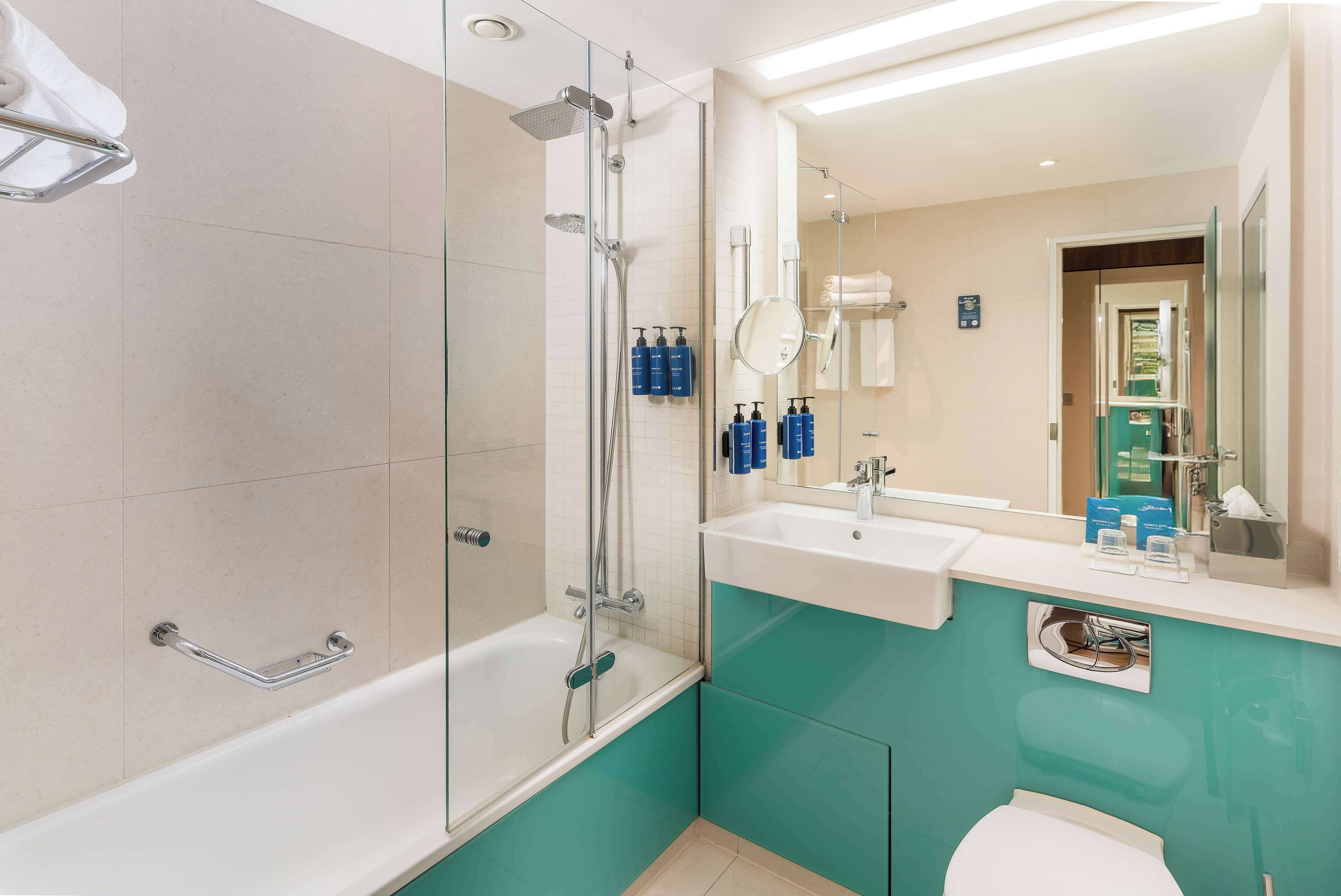 Une salle de bain moderne avec une douche à parois de verre, une baignoire blanche, un lavabo avec un miroir au-dessus, et des murs de couleur turquoise.