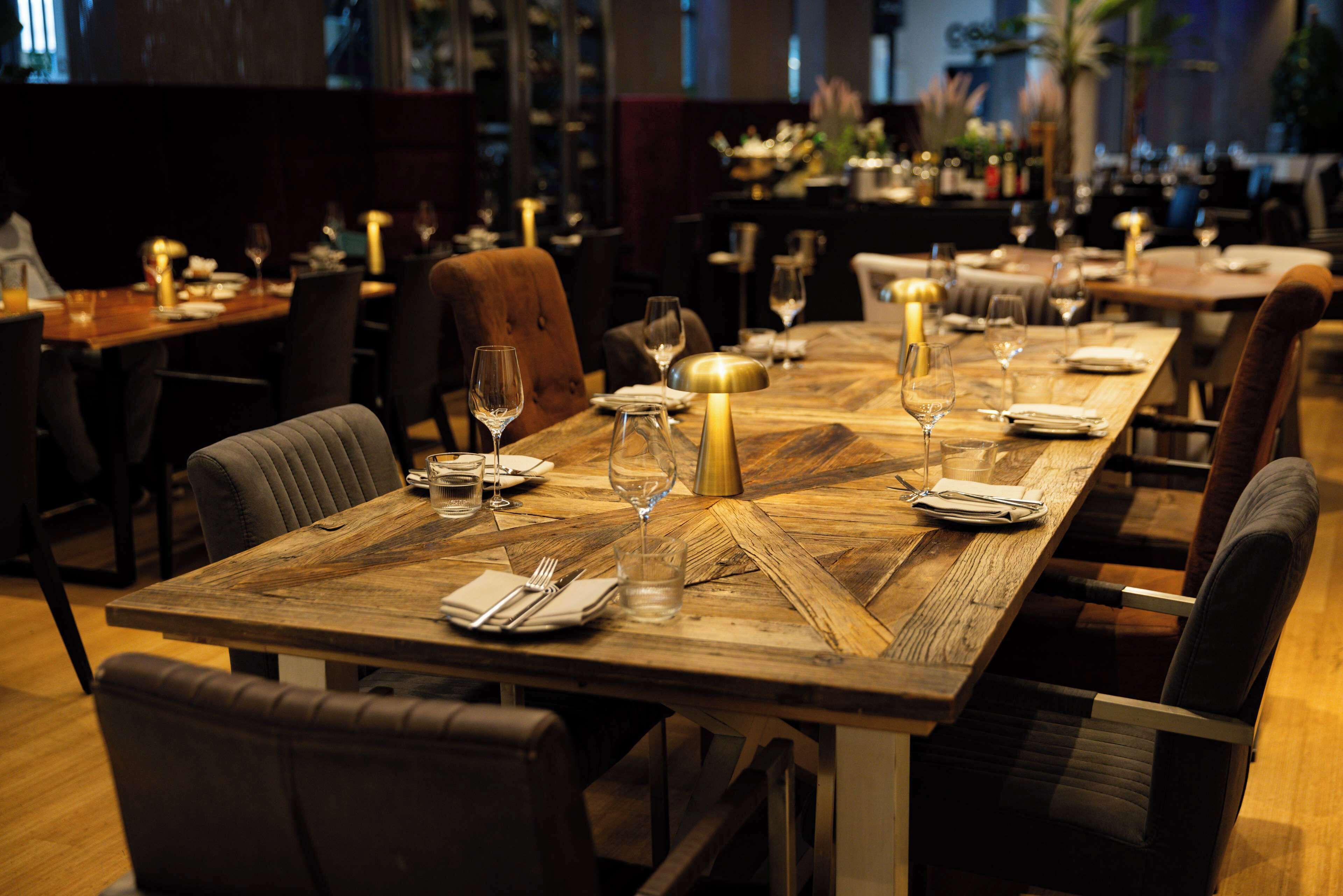 A restaurant with wooden tables set for dining, chairs, and candles.