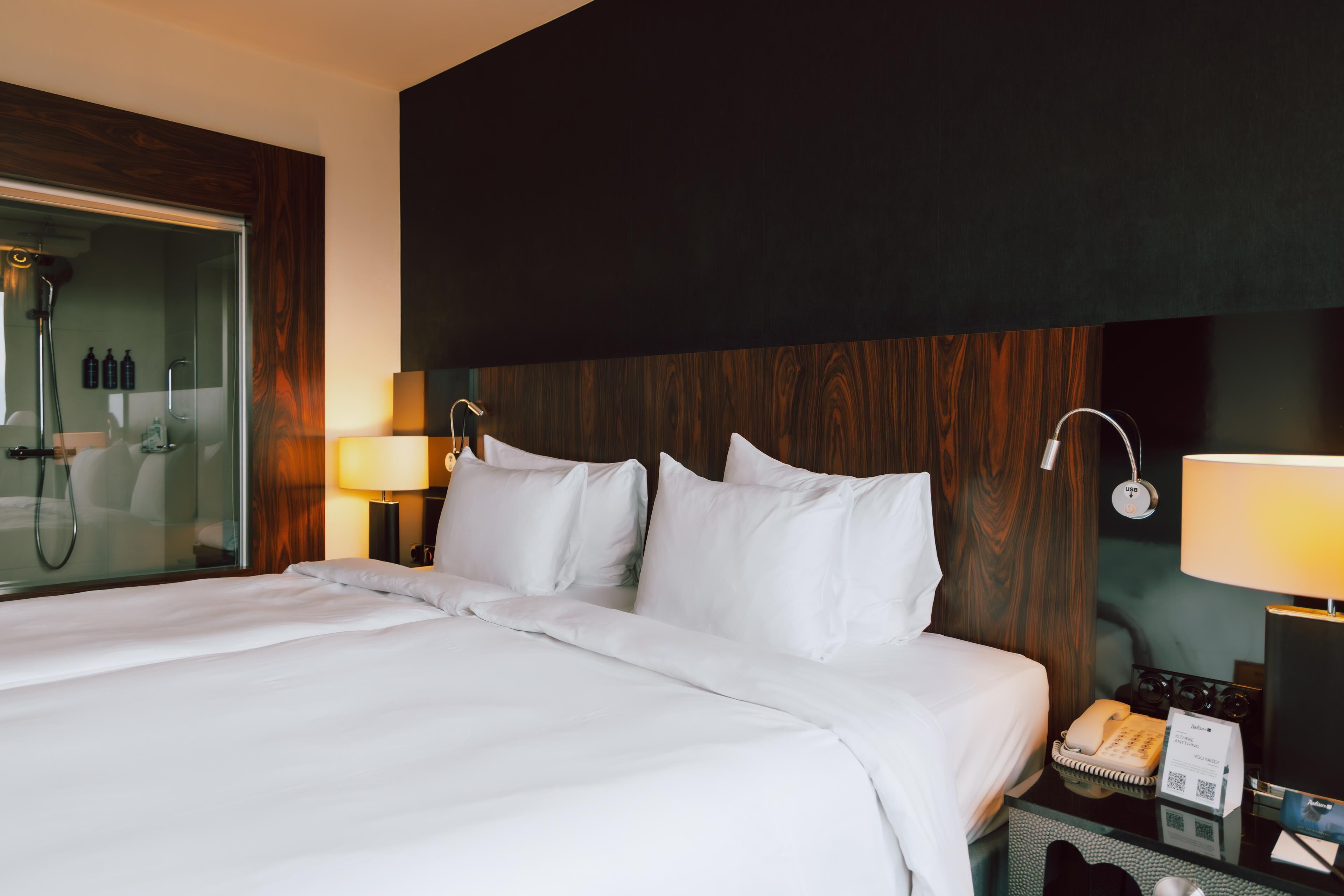 Een hotelkamer met een groot bed, bedlampen, een telefoon en een minibar.