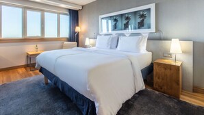 Ein Hotelzimmer mit einem großen Bett, zwei Nachttischen, einem Wandbild und einem Fenster mit Vorhängen.