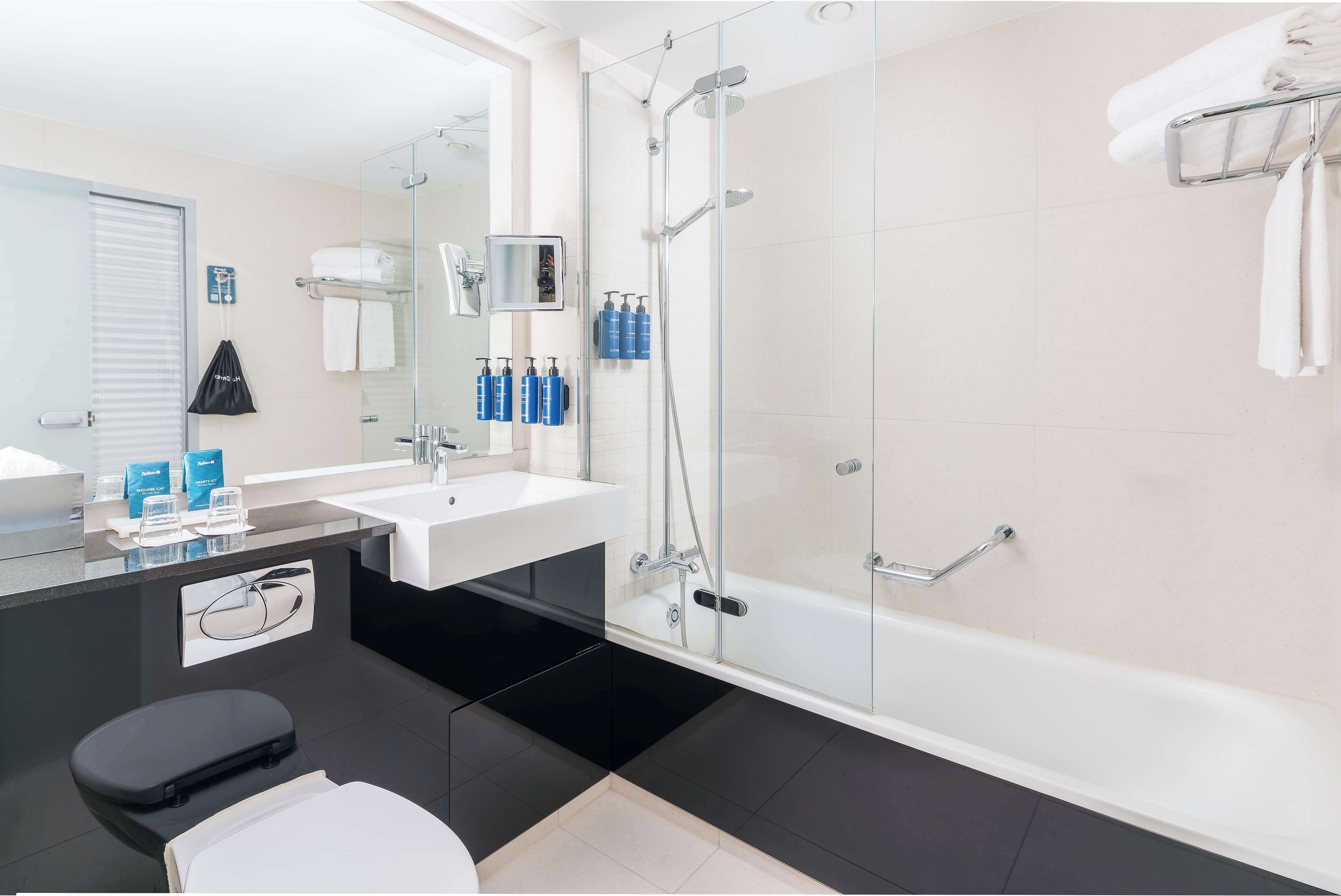 Une salle de bain moderne avec une douche à parois de verre, une baignoire blanche, des toilettes noires et un grand miroir au-dessus du lavabo.