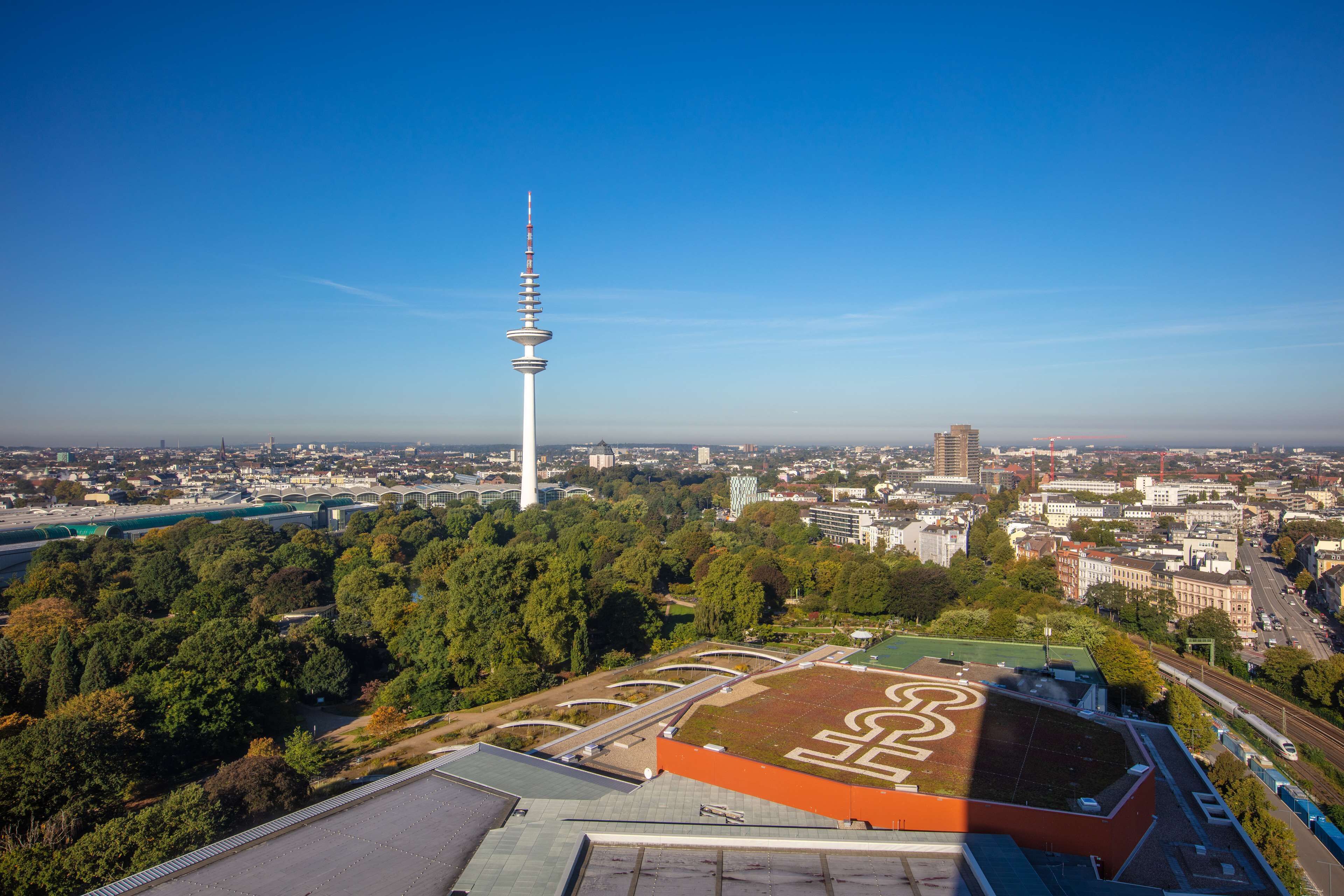 Eine Stadtansicht mit einem markanten Turm, einem Sportplatz und umgebenden Gebäuden.