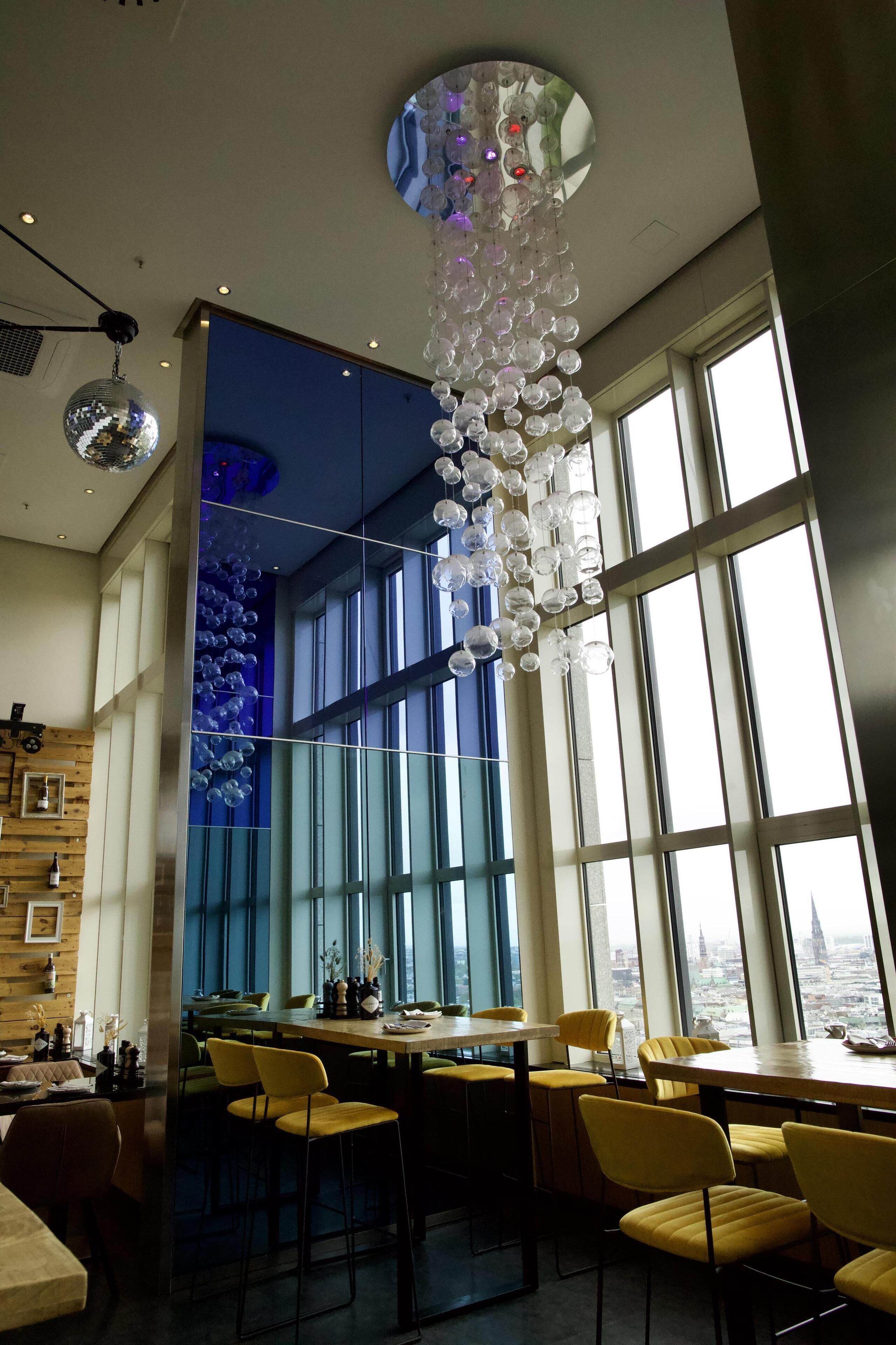 A modern dining area with large windows, yellow chairs, and a unique chandelier.