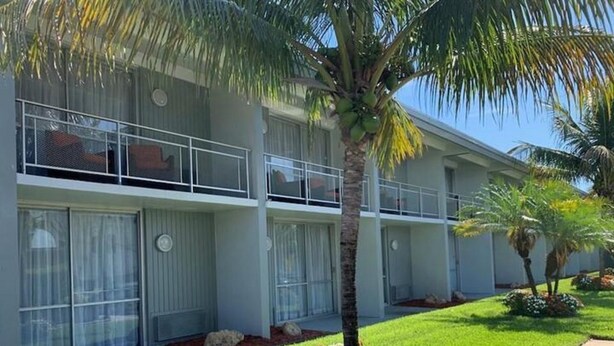 A modern hotel with a two-story structure, large windows, and a well-maintained lawn with palm trees.