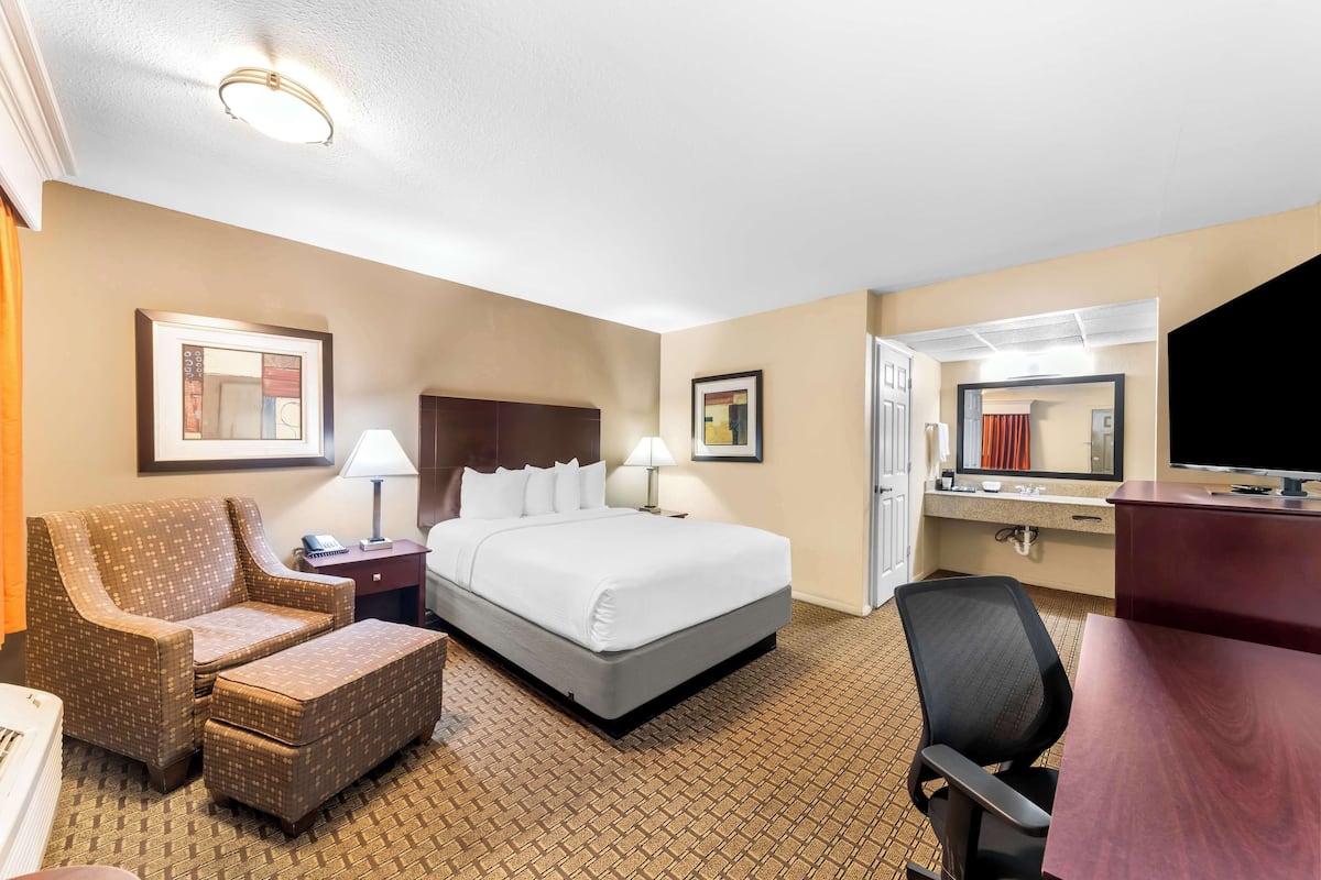 Ein Hotelzimmer mit Bett, Schreibtisch, Stuhl, Lampe und Fernseher.