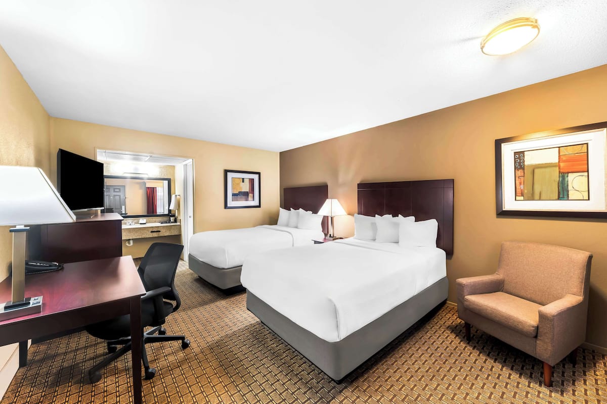 Ein Hotelzimmer mit einem großen Bett, einem Schreibtisch mit Computer, einem Stuhl und einem Fernseher.