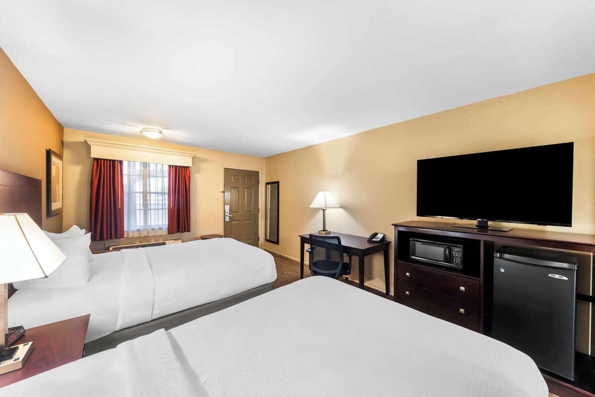 Ein Hotelzimmer mit zwei Betten, einem Schreibtisch mit Lampe, einem Fernseher, einer Mikrowelle und einem Kühlschrank.