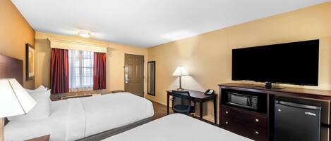 A hotel room with two beds, a desk with a lamp, a television, a microwave, and a refrigerator.