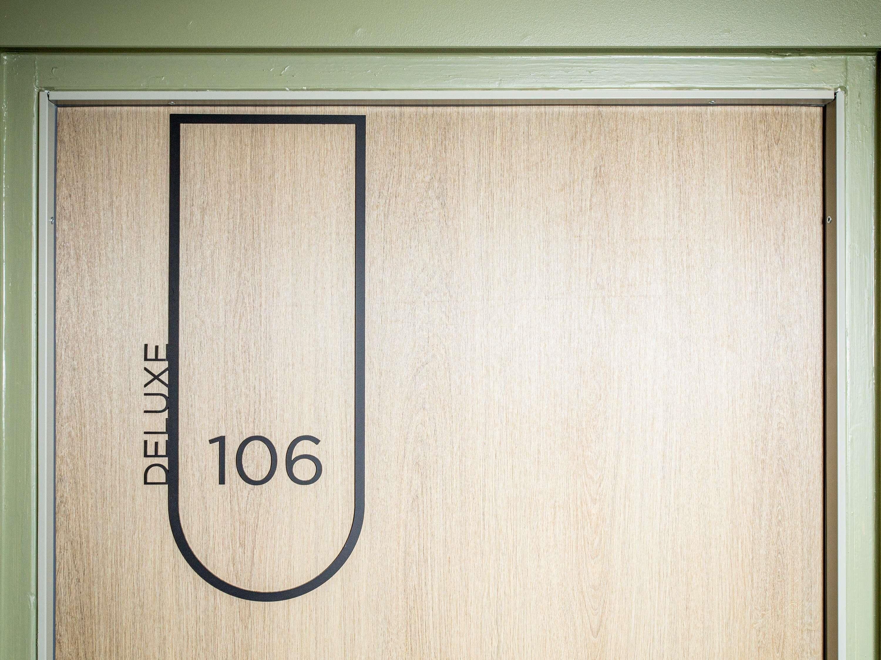 A wooden door with a black outline and the text "DELUXE 106" on it.