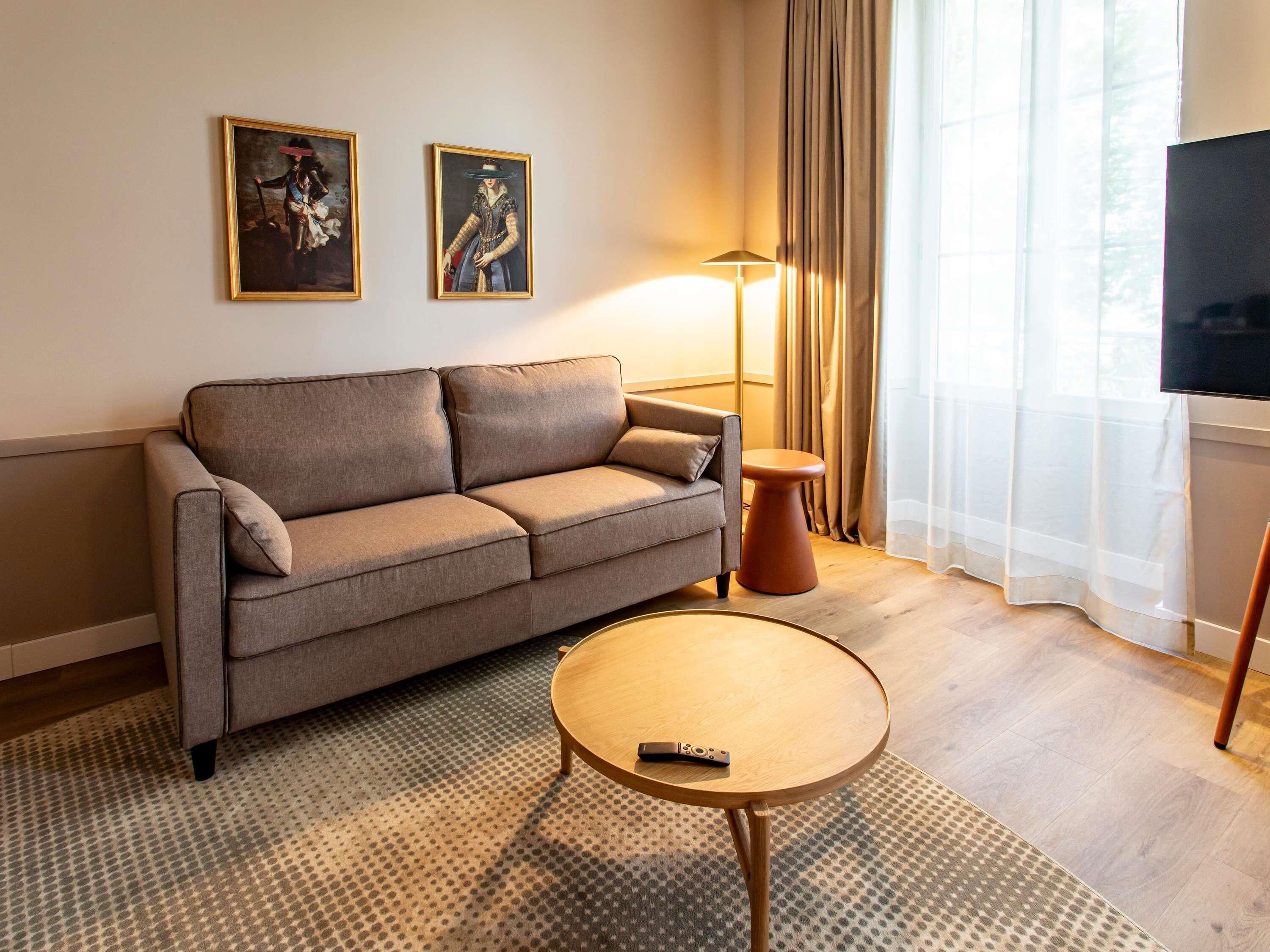 Un salon moderne avec un canapé, une table basse ronde, un lampadaire et deux œuvres d’art encadrées accrochées au mur.