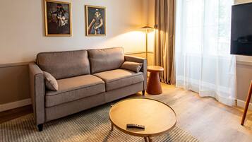 A modern living room with a sofa, a round coffee table, a floor lamp, and two framed artworks on the wall.