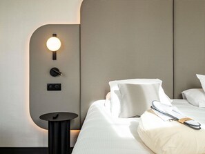 A hotel room with a checkered headboard, a bedside table with a lamp, and a bed with white bedding and a pillow.
