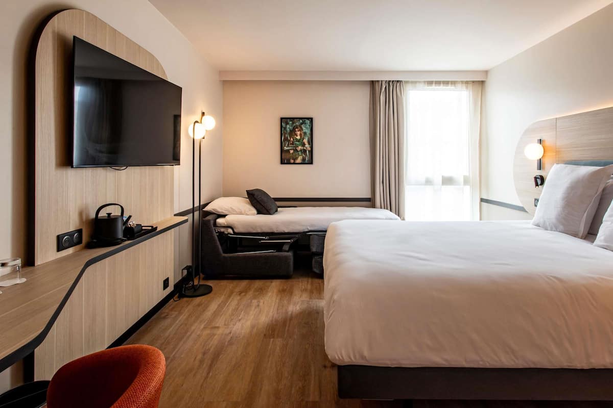 Une chambre d’hôtel équipée d’une télévision, de deux lits, d’un bureau, d’une chaise et d’un tableau au mur.