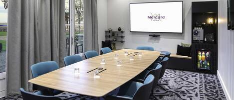 A conference room with a large table, chairs, a projector screen, and a beverage cooler.