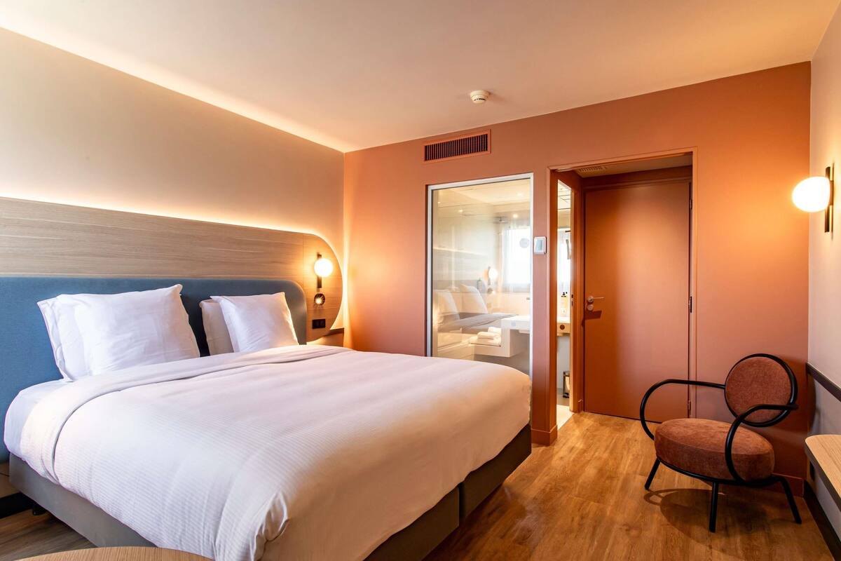 Une chambre d’hôtel comprenant un lit, des tables de chevet, une chaise et une porte donnant sur une salle de bain.