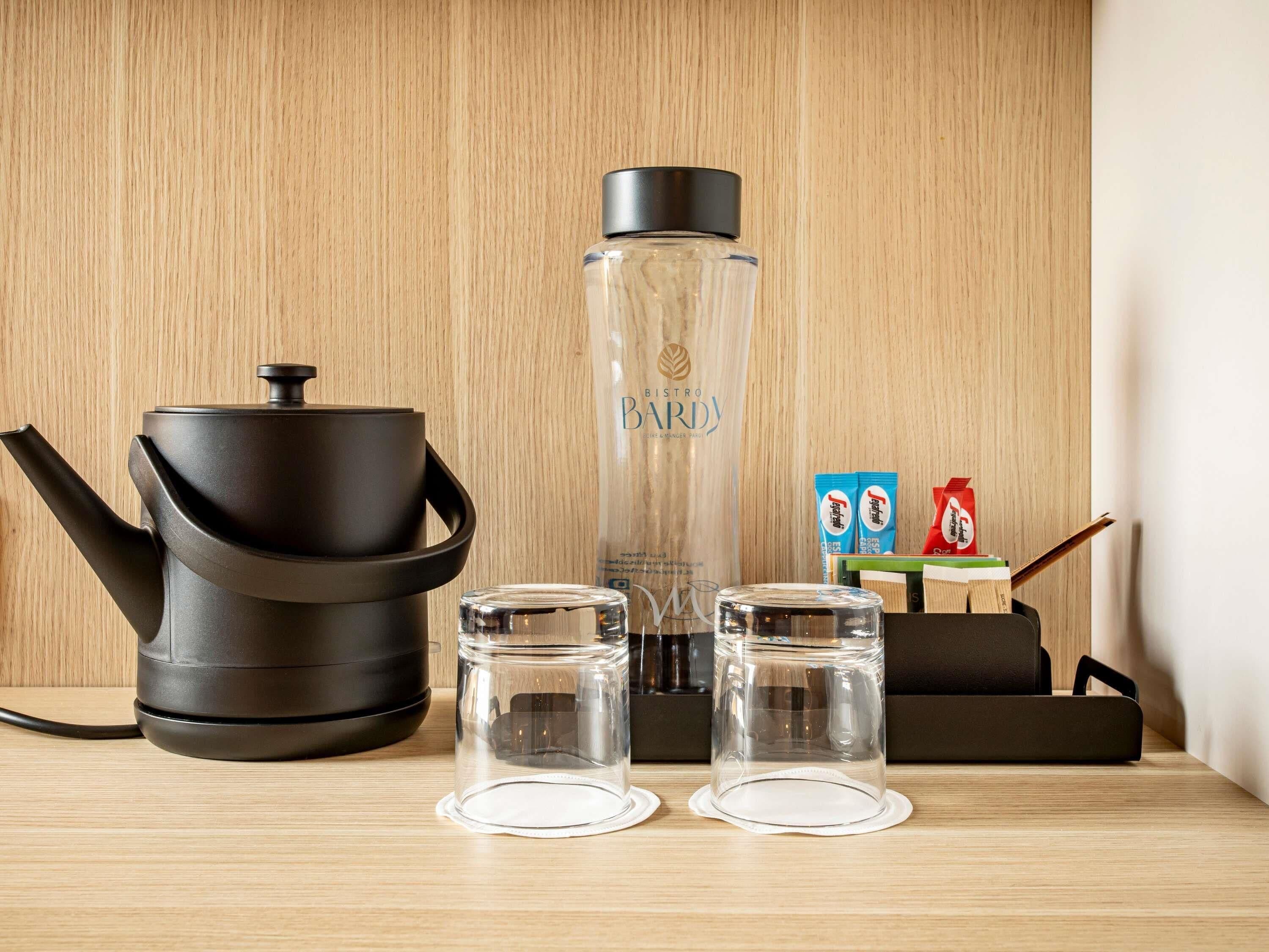 A kitchen setup with a coffee maker, a water bottle, two glasses, and a box of coffee pods.