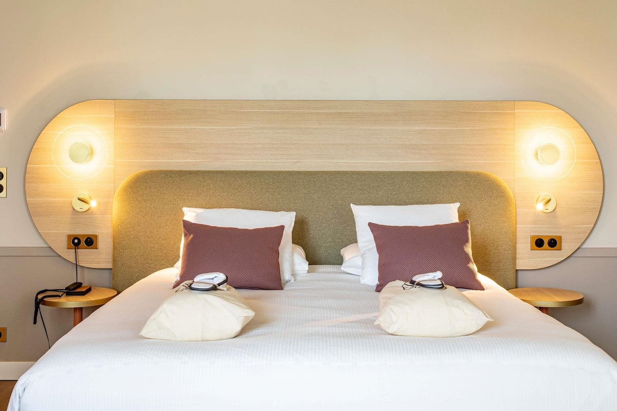 Une chambre d’hôtel avec un grand lit, deux tables de chevet et des lampes fixées au mur.