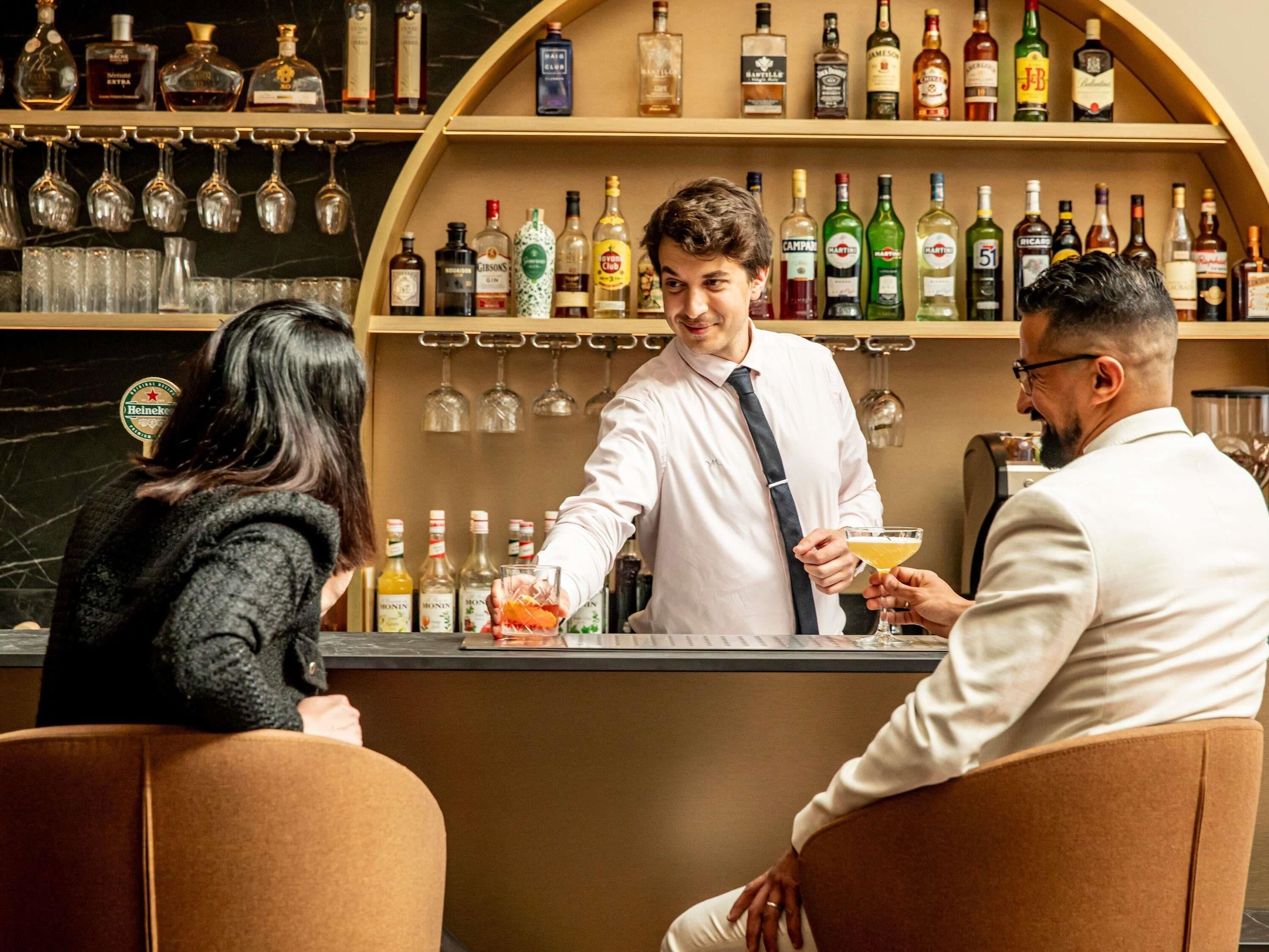 Un espace bar où un barman sert des boissons aux clients assis.