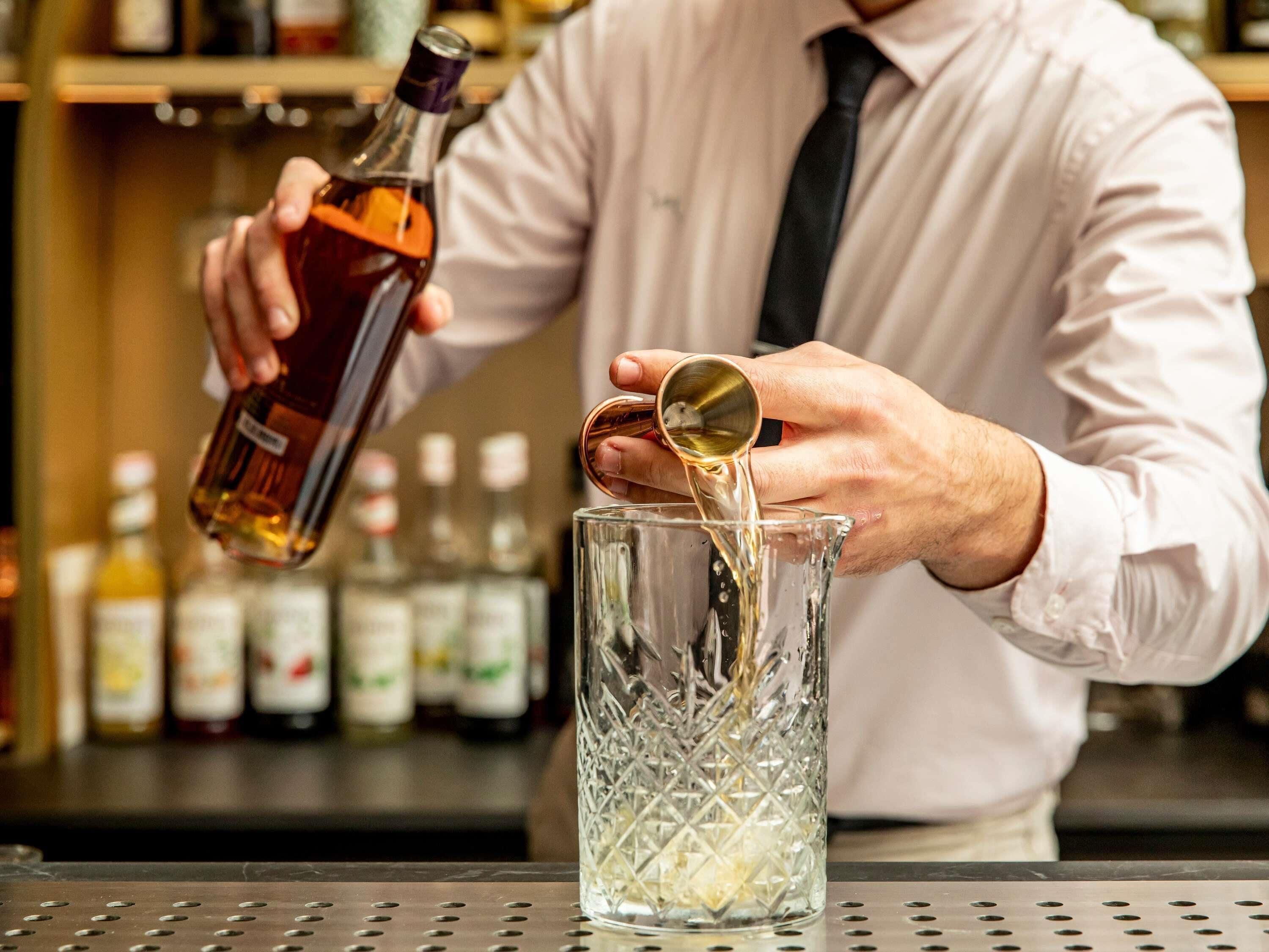 A bartender pouring a drink into a crystal glass.