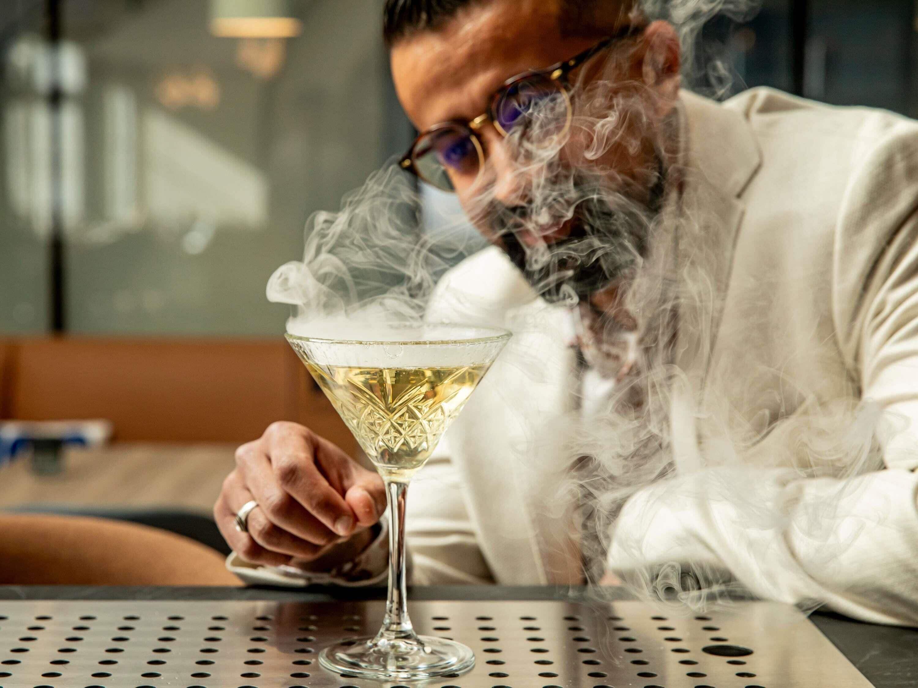 A person sitting at a table with a martini glass emitting smoke.
