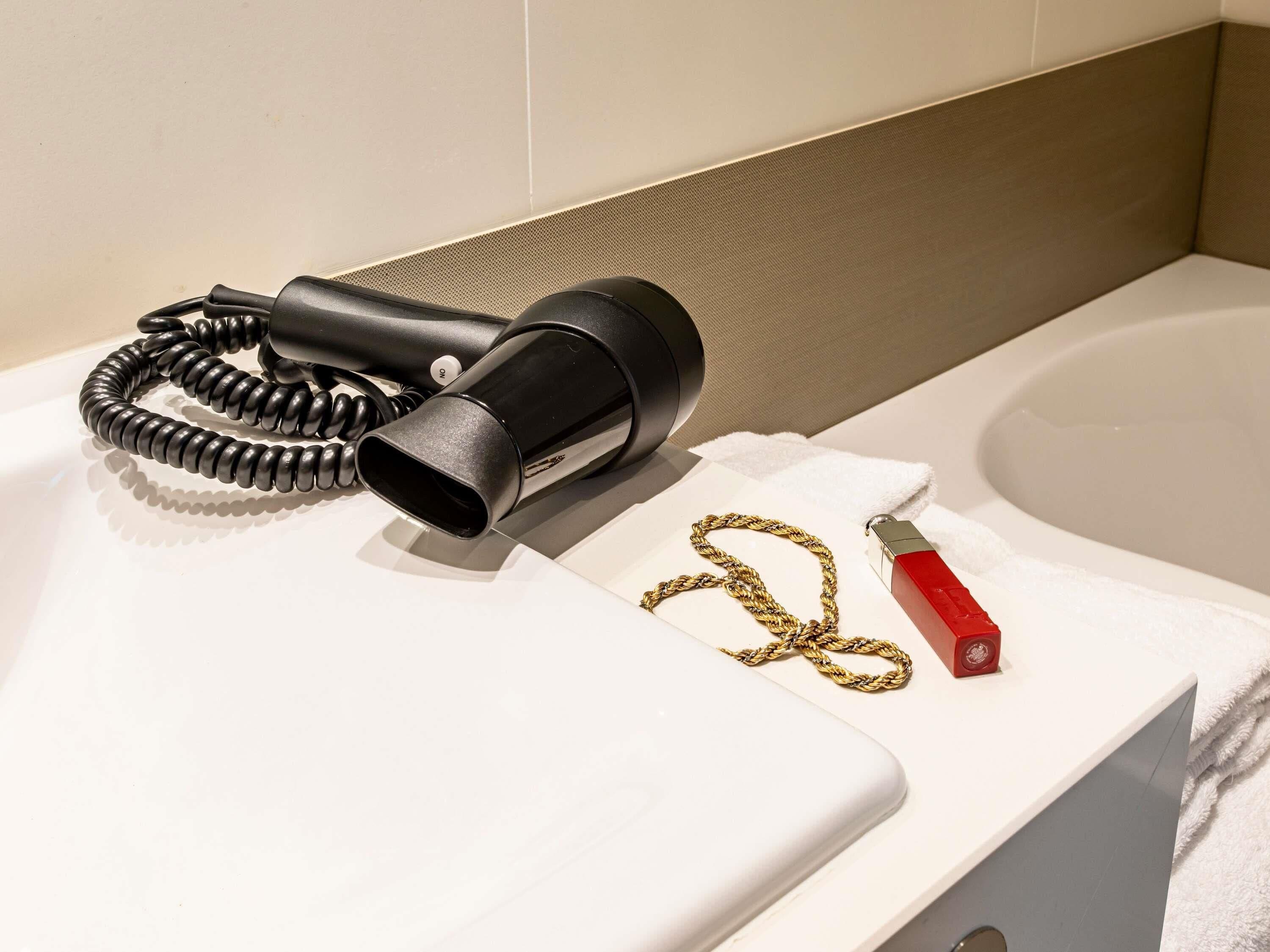 A bathroom with a hairdryer, a gold chain, and a red object on a white countertop.