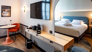 Una habitación de hotel con una cama, un escritorio con cafetera, televisor, silla y espejo.