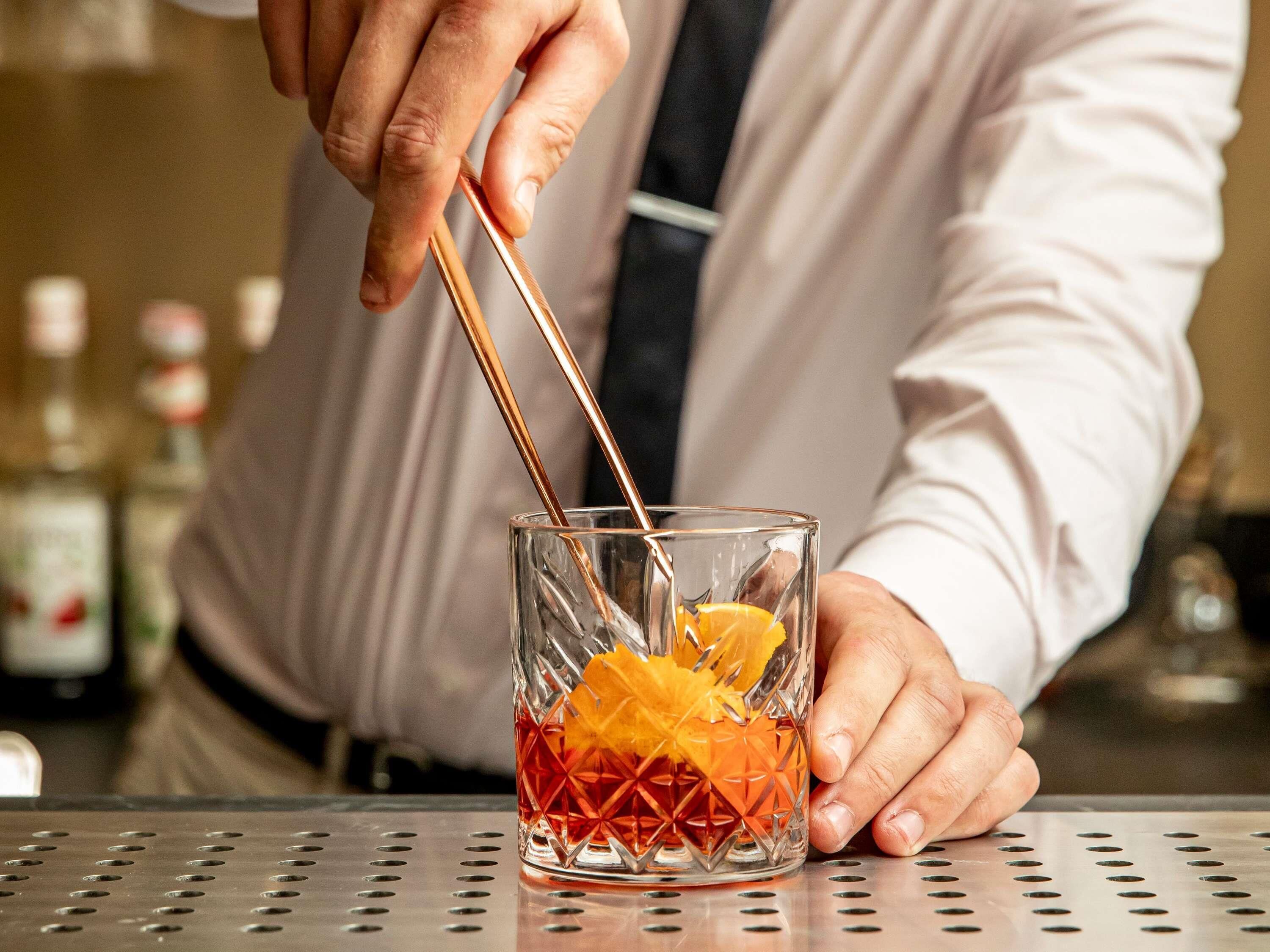 A person stirring a drink in a glass with a copper straw.