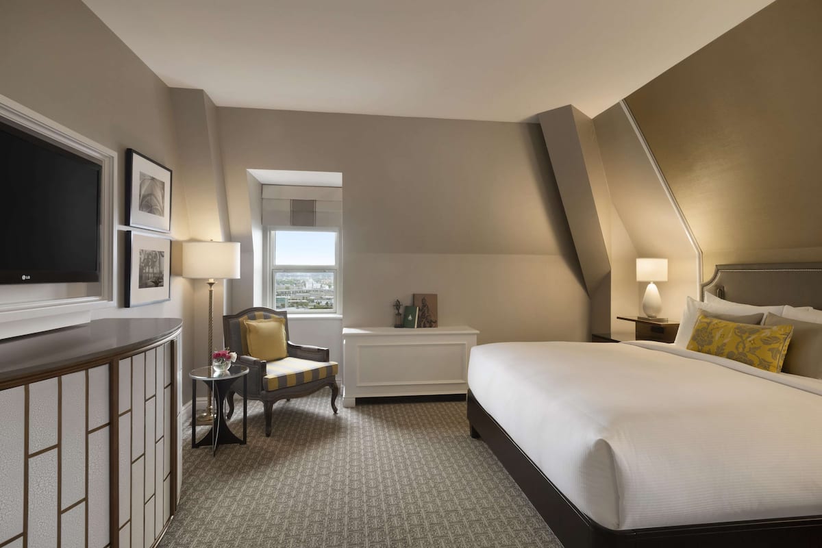 A hotel room with a bed, a desk, a chair, a TV, a window, and a view of the city.