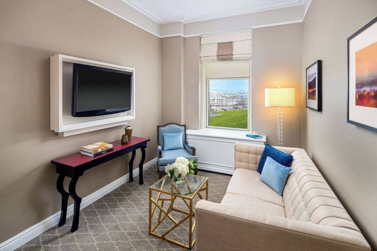A living room with a flat-screen TV, a sofa, a chair, a coffee table, and a window with a view of a building.