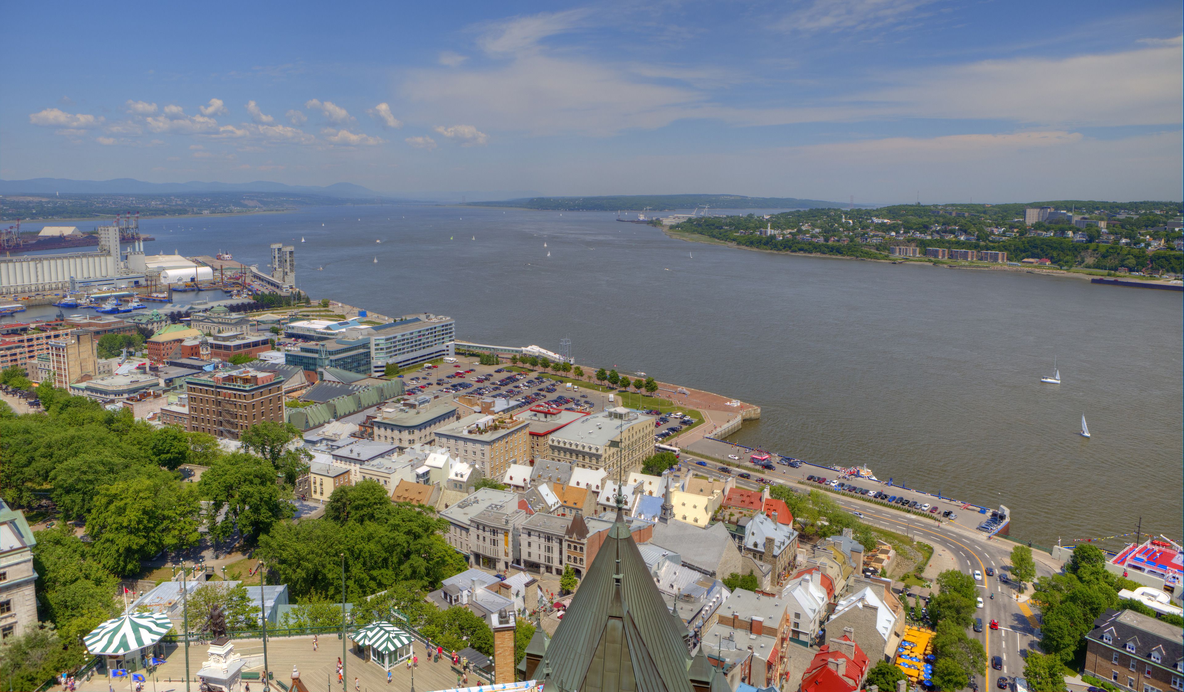 A waterfront cityscape with a mix of historic and modern buildings, a marina, and a bridge in the distance.