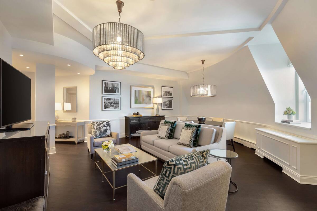 A modern living room with a sofa, coffee table, and TV. There are framed pictures on the wall and a chandelier.