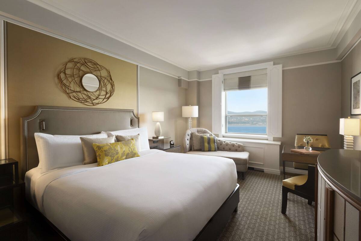 A hotel room with a large bed, a desk, a chair, a window with a view, and a decorative wall piece.