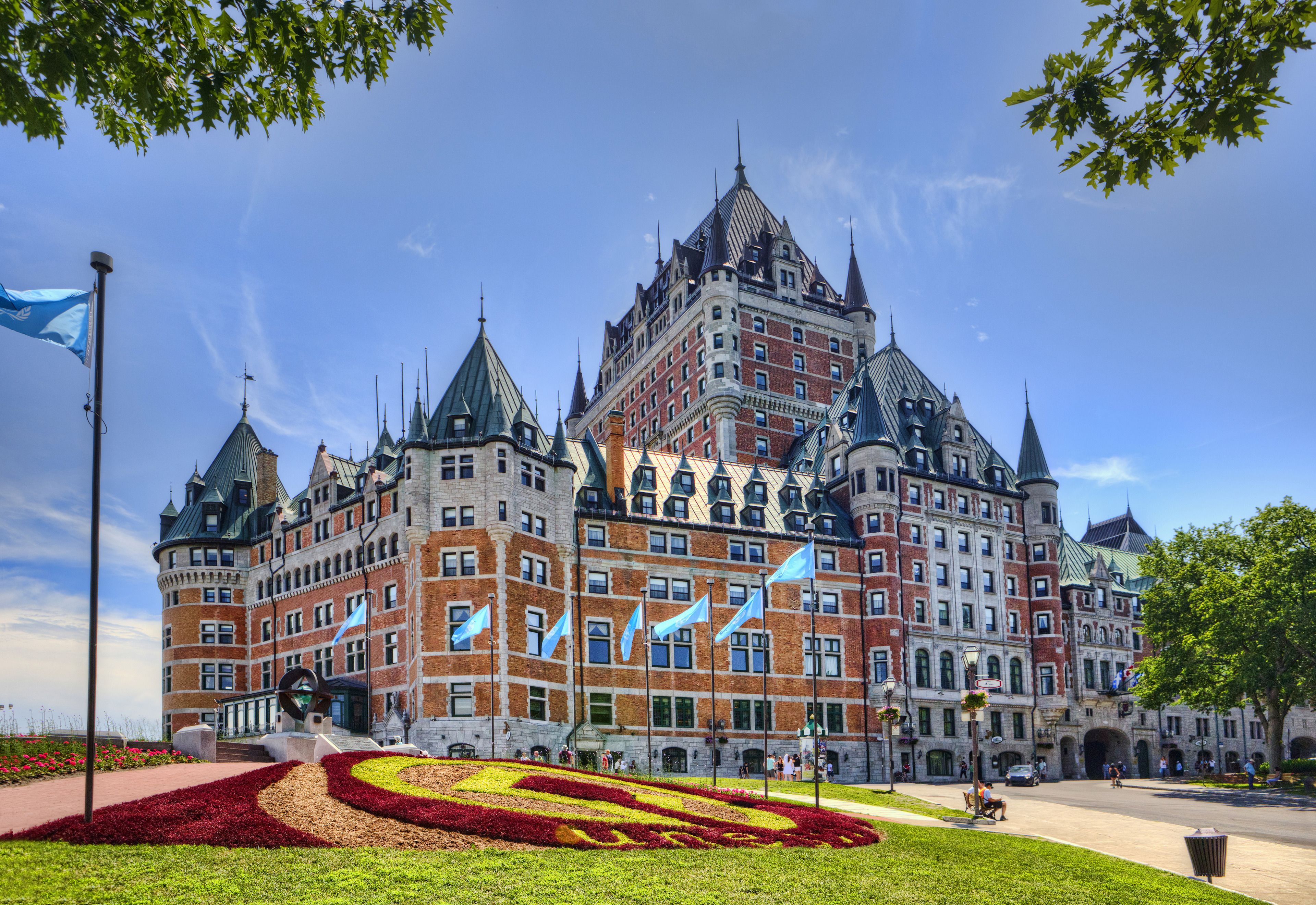Un grand bâtiment historique, doté de nombreuses tours et de drapeaux, entouré de jardins bien entretenus et surplombant un ciel dégagé.