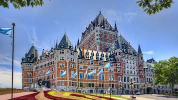 Un grand bâtiment historique, doté de nombreuses tours et de drapeaux, entouré de jardins bien entretenus et surplombant un ciel dégagé.