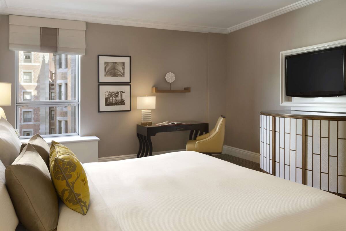 A hotel room with a large bed, a desk with a chair, a television, and framed pictures on the wall.
