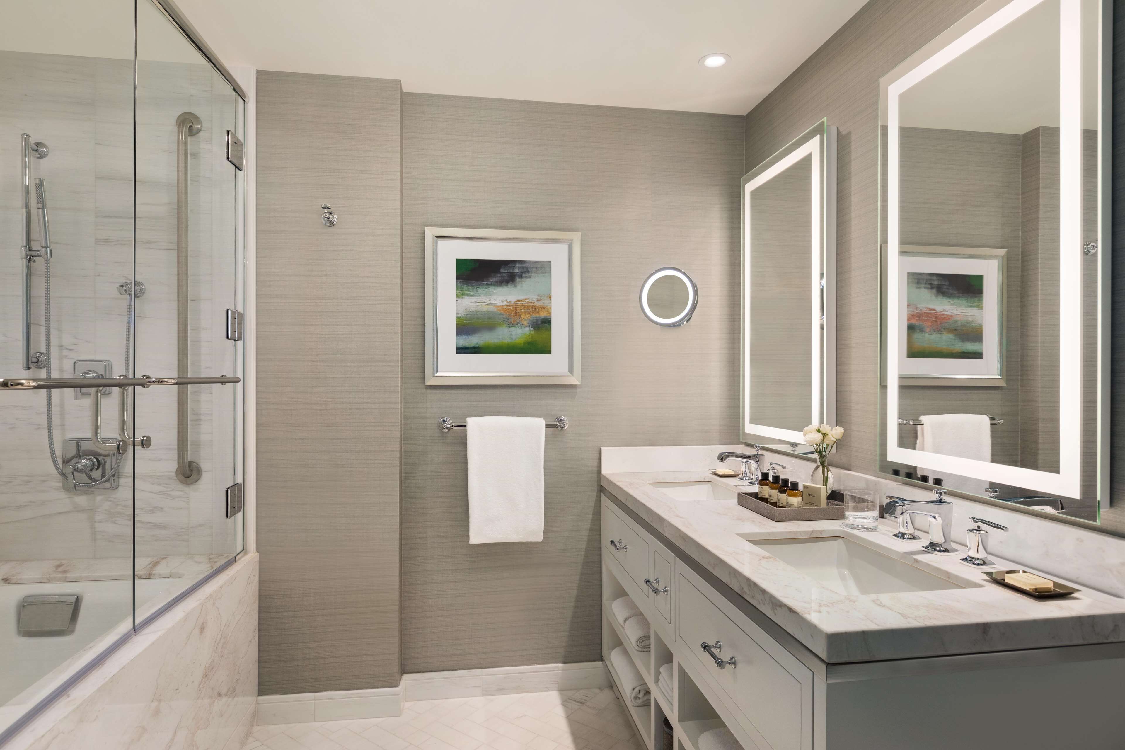 A modern bathroom with a glass shower enclosure, a double sink vanity, and two framed artworks on the wall.
