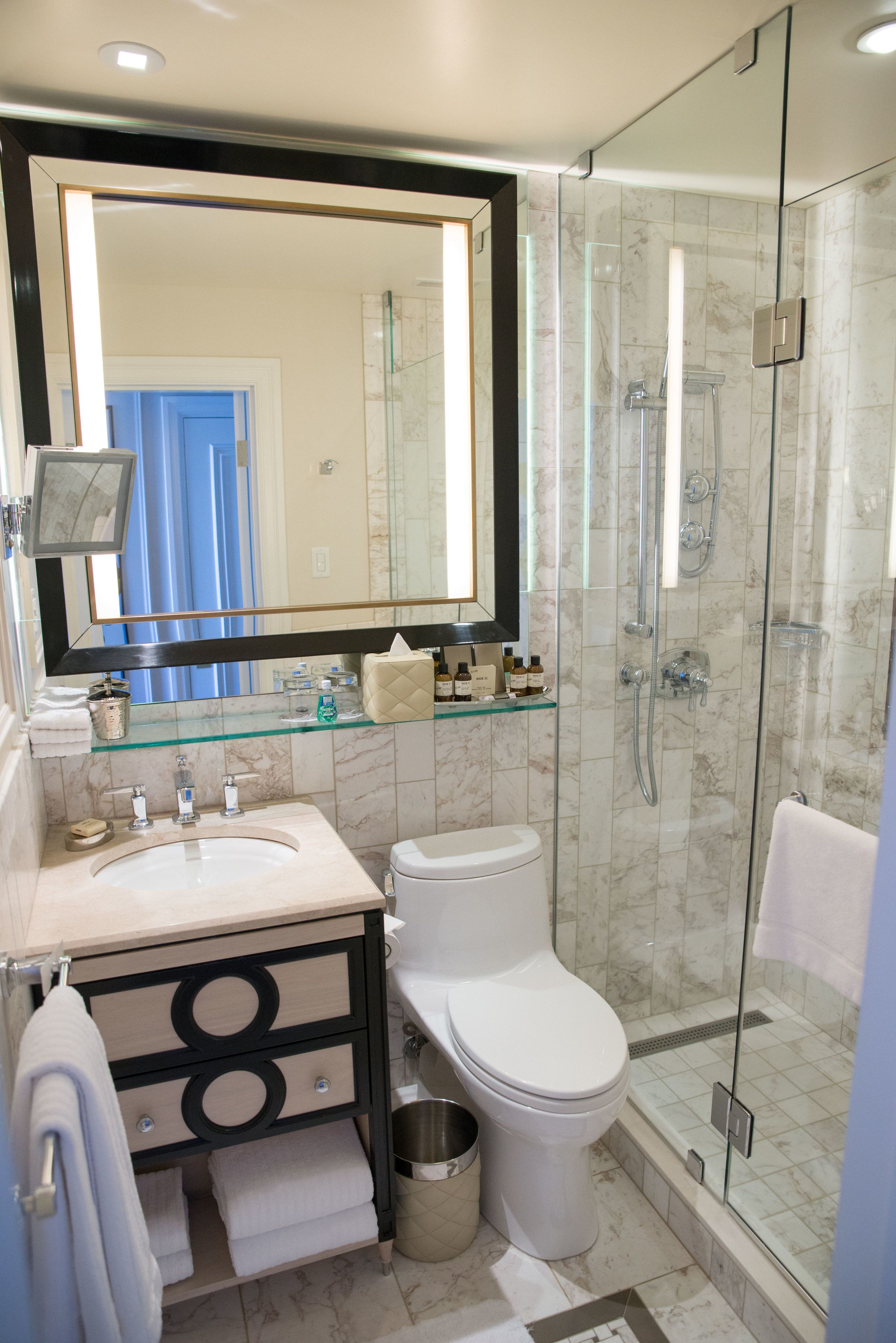 Une salle de bain moderne dotée d’une douche à parois de verre, d’un grand miroir et d’un meuble-lavabo avec un évier et des toilettes.