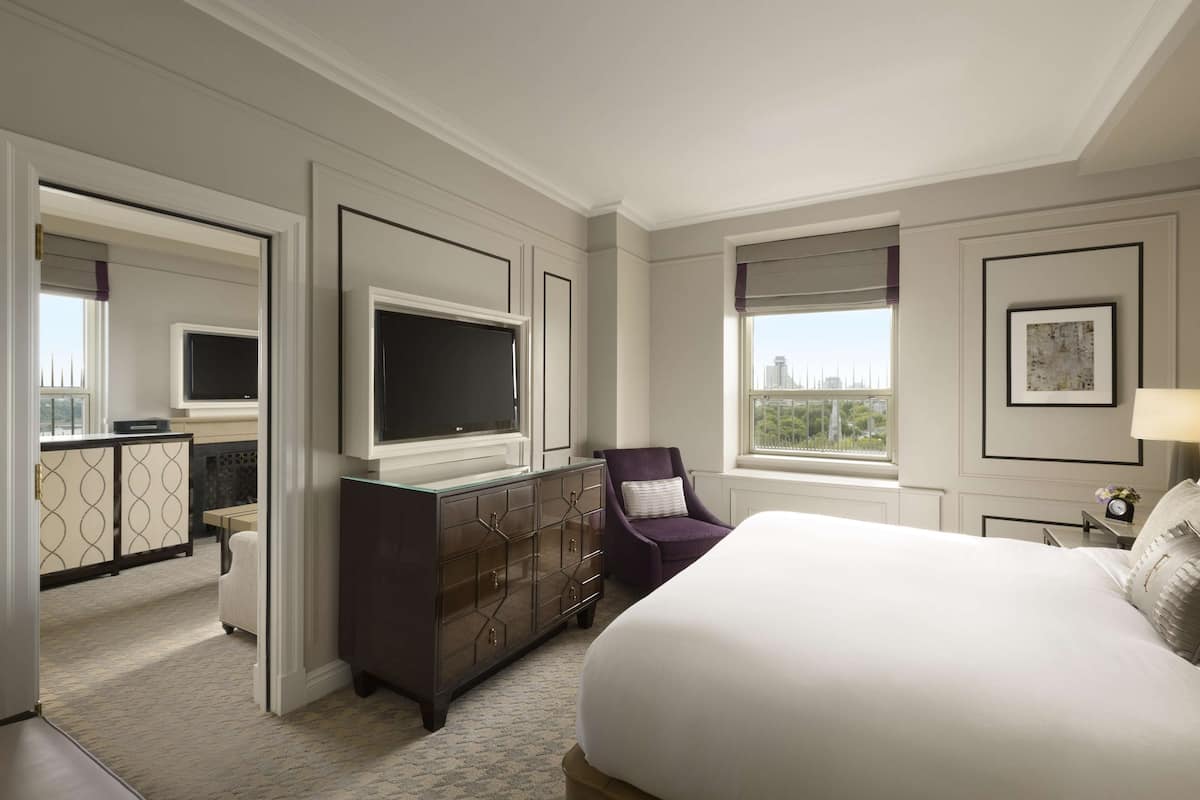 A hotel room with a large bed, a TV, a dresser, a chair, and a window with a city view.