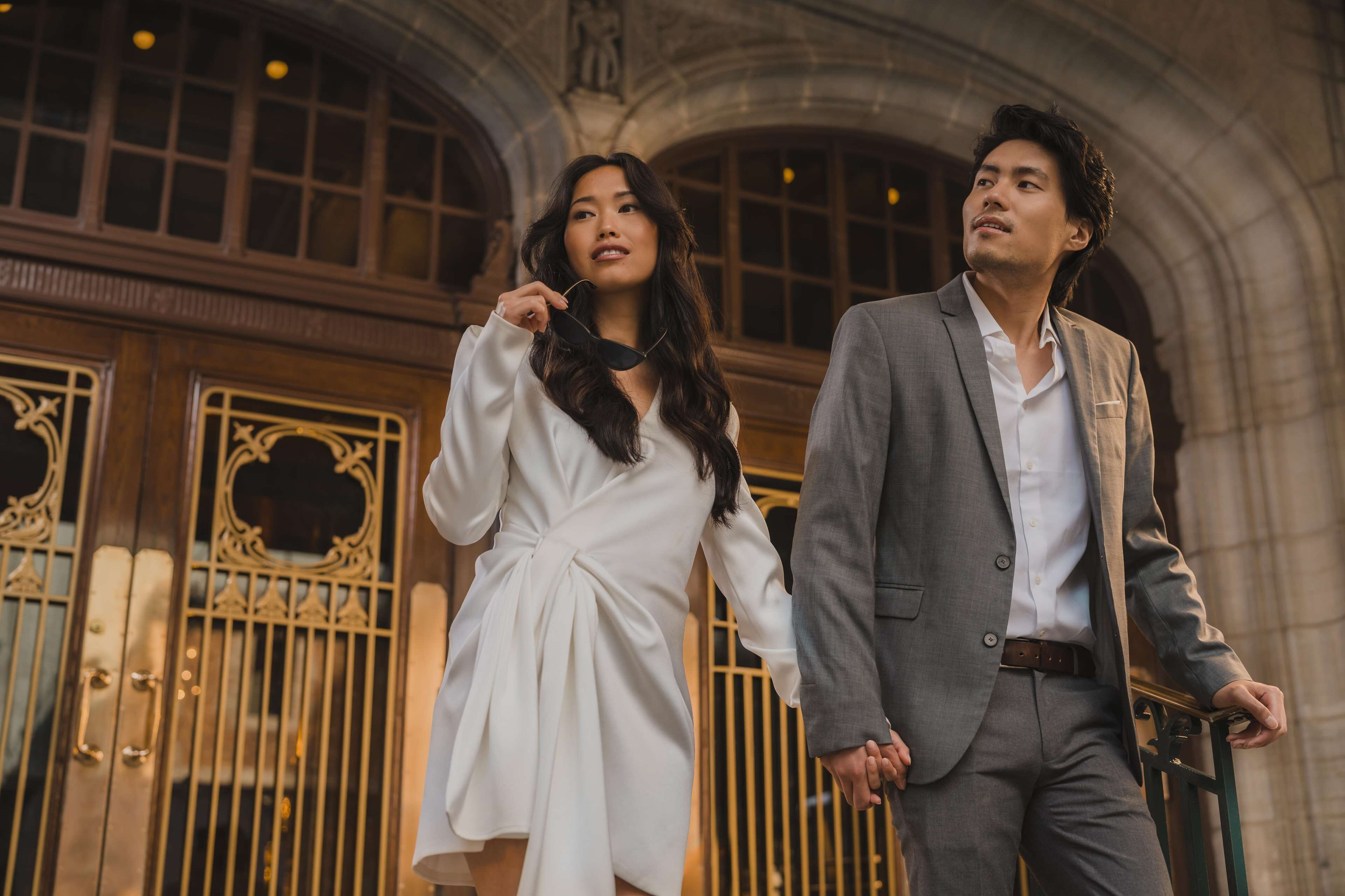 A couple standing in front of a grand building with ornate gates.