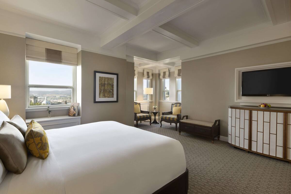 A hotel room with a large bed, a television, a desk, and a view of the city.
