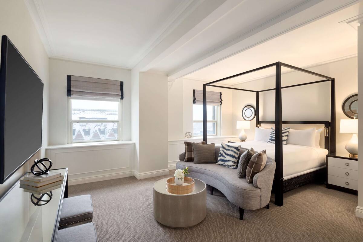A bedroom with a four-poster bed, a sofa, a TV, and a round coffee table.