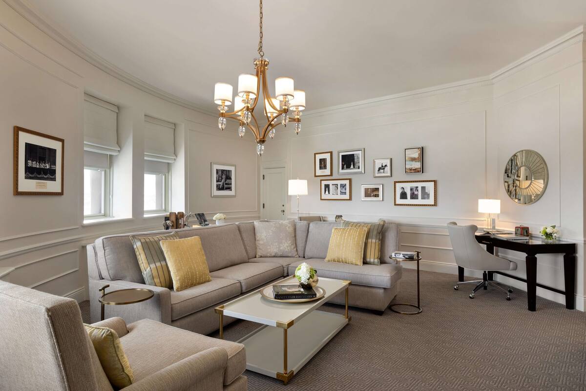 A spacious living room with a large beige sectional sofa, a coffee table, a desk with a chair, and a chandelier.