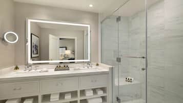 A modern bathroom with a large mirror, two sinks, a shower, and a vanity with storage.