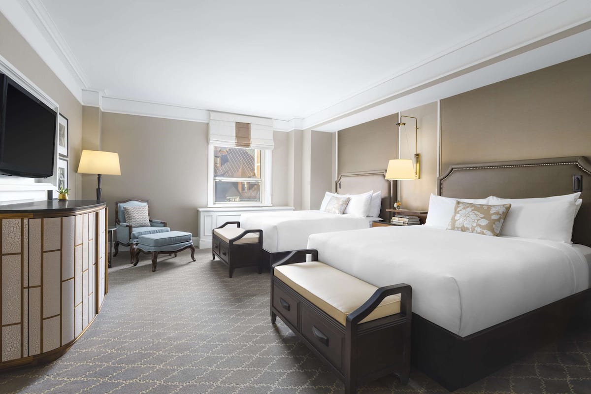A hotel room with a large bed, a smaller bed, a desk, a chair, and a television.