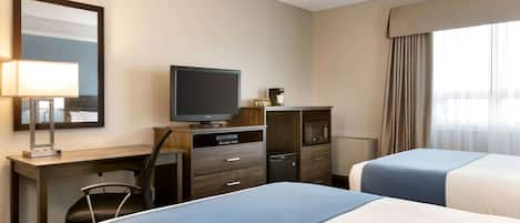 Habitación de hotel con dos camas, un escritorio con televisor, una silla, lámpara de escritorio, microondas y minibar.