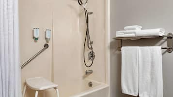 A bathroom with a walk-in shower, a white stool, and a towel rack with folded towels.