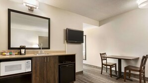 A hotel room with a kitchenette, a large mirror, a flat-screen TV, and a dining area with two chairs.