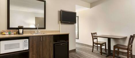 Habitación de hotel con kitchenette, un espejo grande, televisión de pantalla plana y comedor con dos sillas.