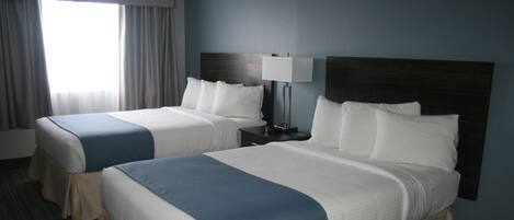 Una habitación de hotel con dos camas, una mesita de noche con lámpara y un ventanal con cortinas.