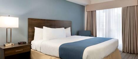 A hotel room with a large bed, a nightstand with a lamp, and a window with curtains.